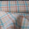 A close-up of the Multi Gingham 100% Linen Fabric showcasing its fine, yarn-dyed plaid pattern in blues, peaches, and creamy oatmeal