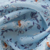 Blue Floral Linen Fabric, lightweight 135 GSM, with delicate white and orange flowers and blue and purple foliage on a soft blue background, ideal for summer dresses and home decor