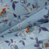 Blue Floral Linen Fabric, lightweight 135 GSM, with delicate white and orange flowers and blue and purple foliage on a soft blue background, ideal for summer dresses and home decor