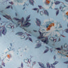 Blue Floral Linen Fabric, lightweight 135 GSM, with delicate white and orange flowers and blue and purple foliage on a soft blue background, ideal for summer dresses and home decor