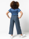 back view of lady wearing blue stripped linen pant made using Fifi Woven Pant sewing pattern, featuring a wide leg design with a smooth front yoke, elastic back, and side pockets, perfect for crepe, linen, and rayon fabrics.