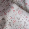 Sheer 100% linen fabric with a loose weave, adorned with a delicate blossom print in soft pinks and grays on an off-white background