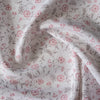 Sheer 100% linen fabric with a loose weave, adorned with a delicate blossom print in soft pinks and grays on an off-white background