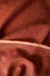 Close-up of burnt orange linen fabric with chocolate damask-style floral print and textured slubby yarn-dyed fibers