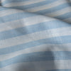 Alternating blue and white yarn-dyed stripes run along the Striped Sky 100% Linen Fabric, showcasing its lightweight, natural feel and soft texture